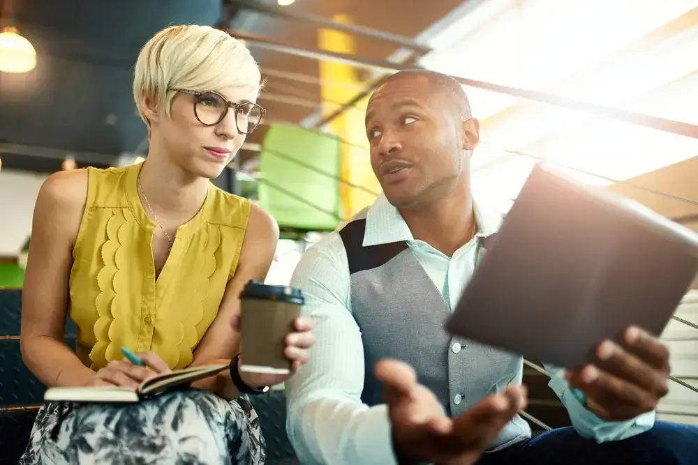 Two creative millenial small business owners solving a high growth problem using a digital tablet while sitting in staircase