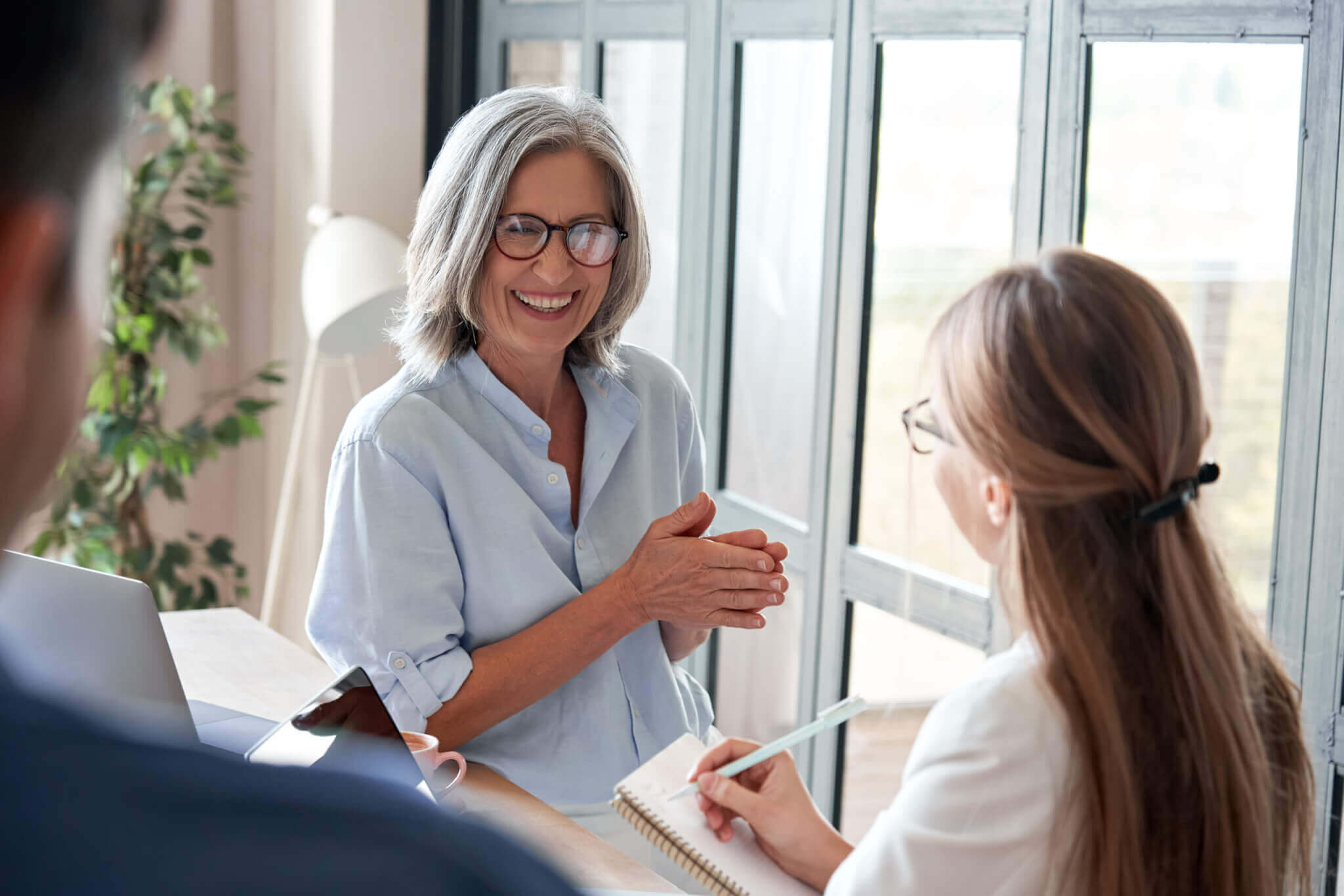 Happy mature old female mentor coach laughing training young interns at group office meeting professional workshop. Cheerful middle aged teacher professor talking to students at university seminar.