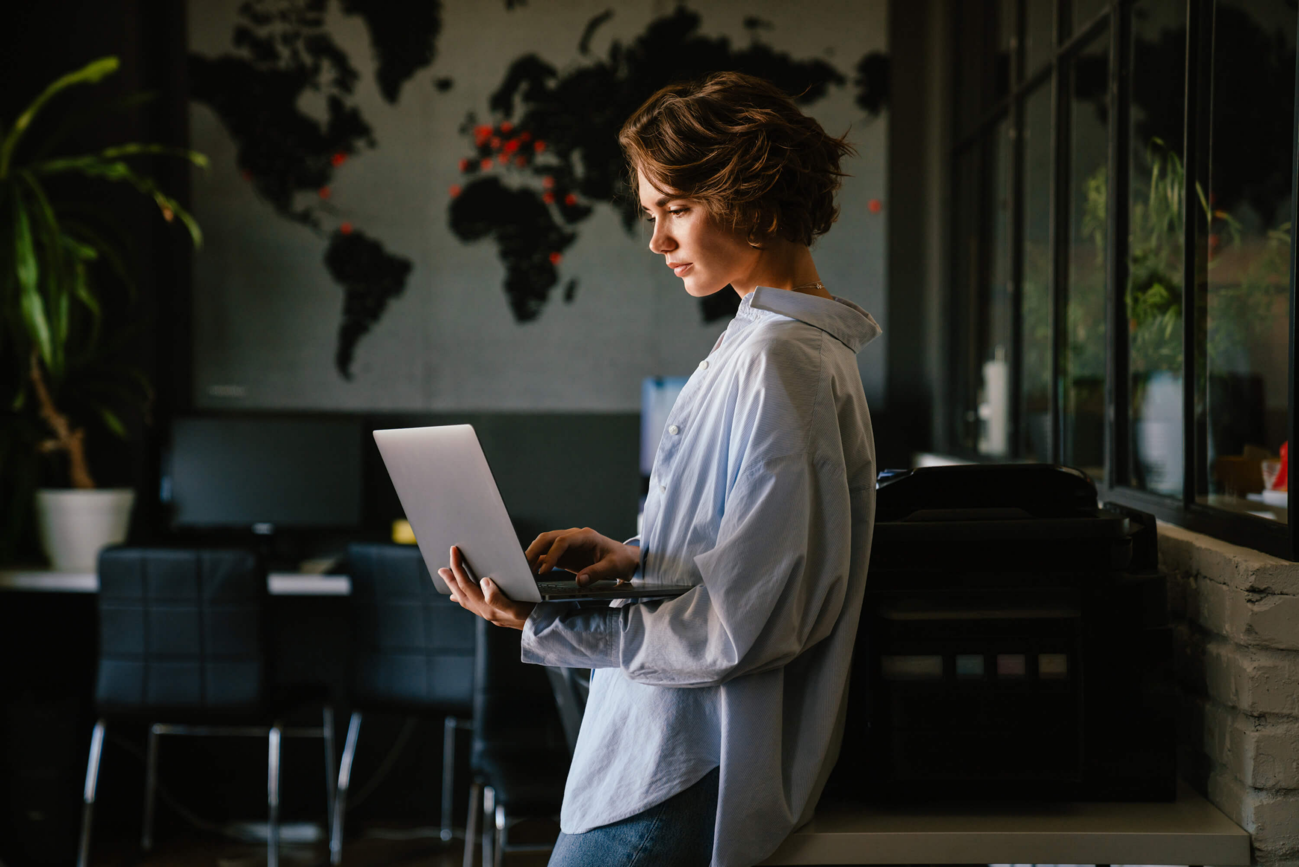 Focused woman using laptop in modern office with a global map in the background