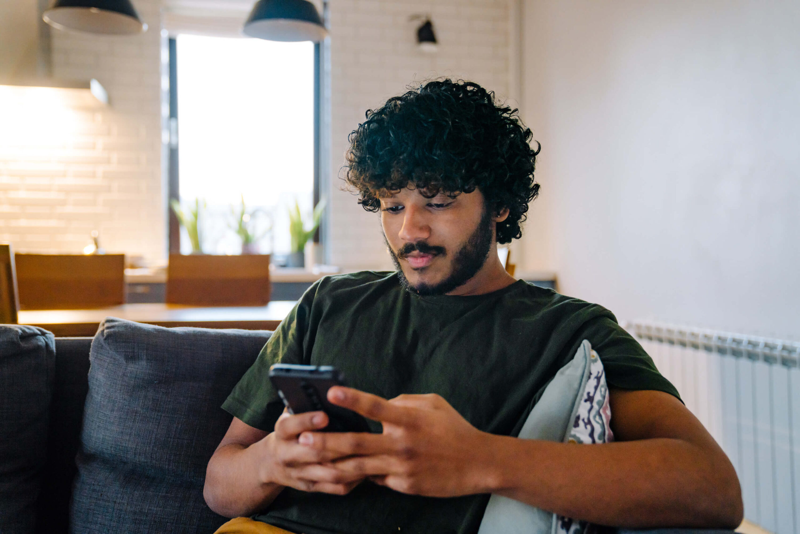 Young man sitting on a couch using a smartphone in a relaxed setting.