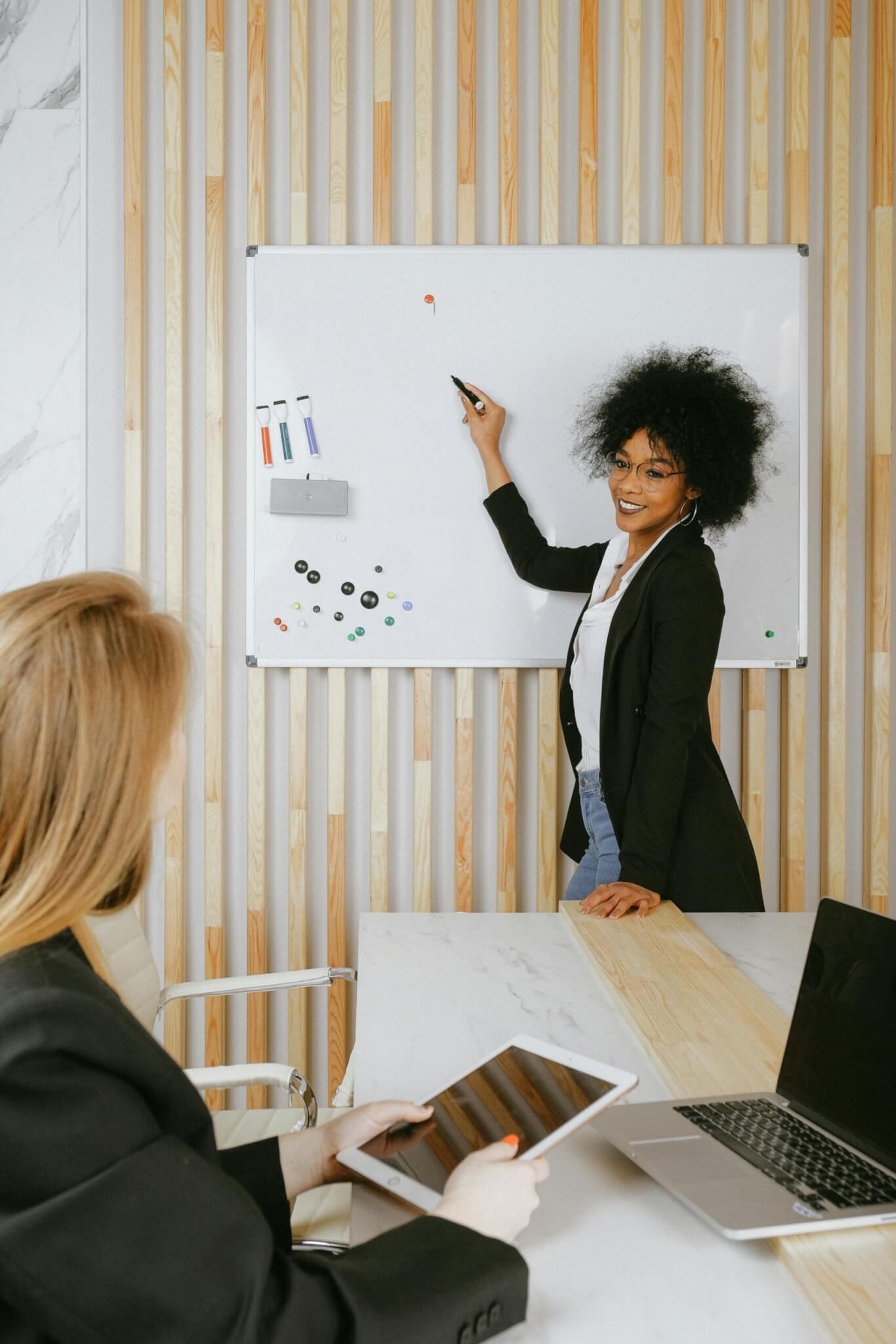 An image of someone at the front of the room pointing to a white board