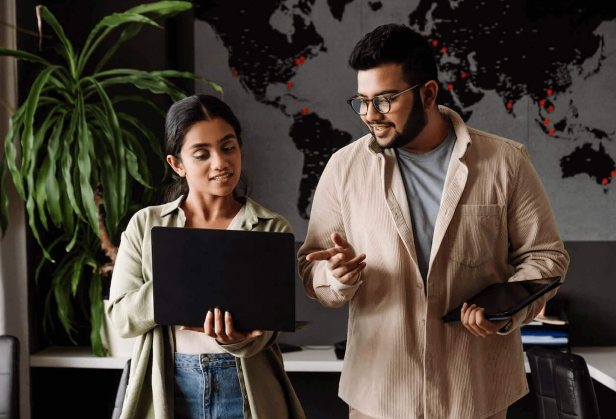 Two professionals collaborating with laptops in front of a world map showing TaskHuman’s global coaching reach